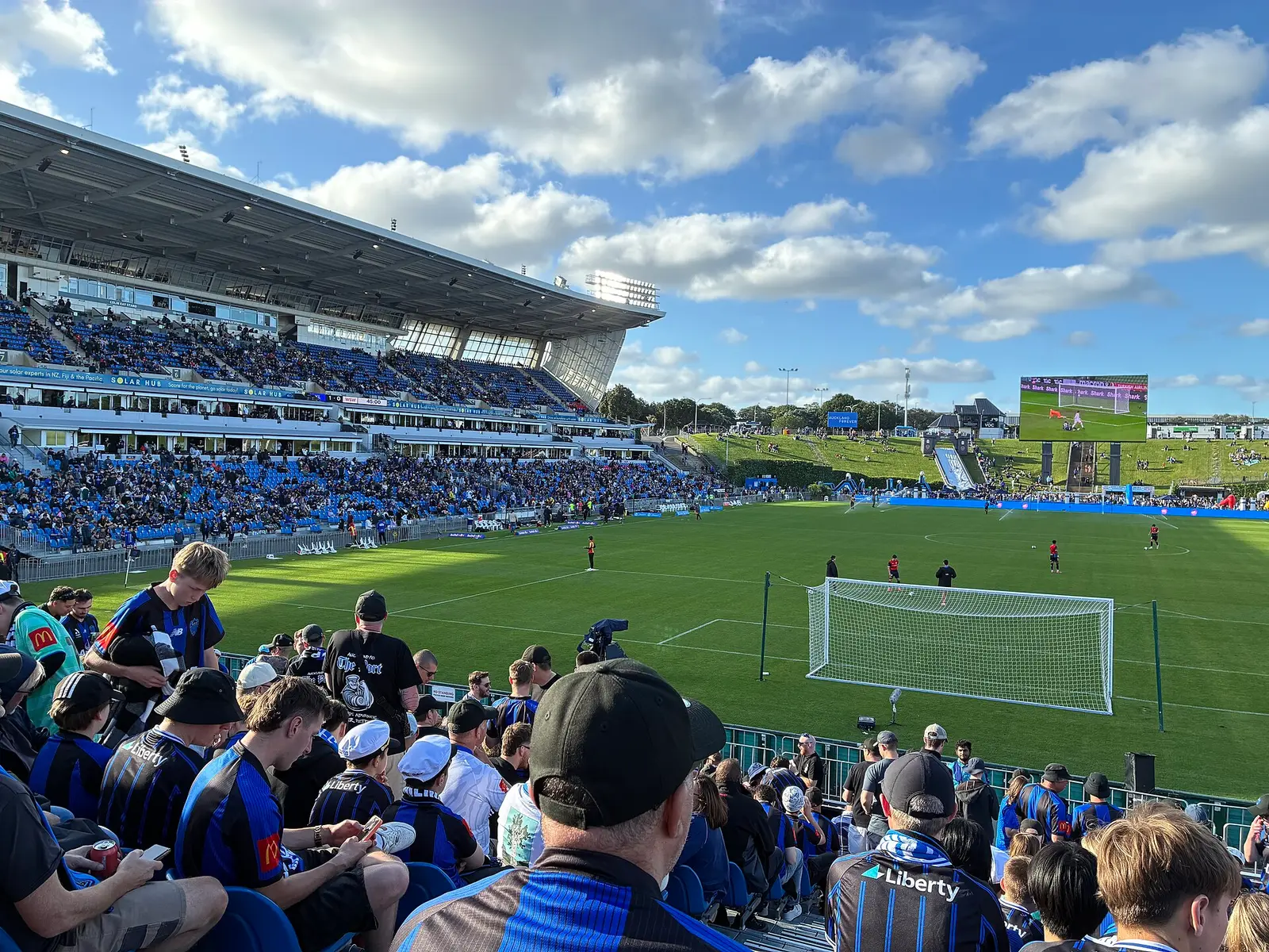 Spectators and the grass pitch at Go Media Stadium in Auckland on a sunny day